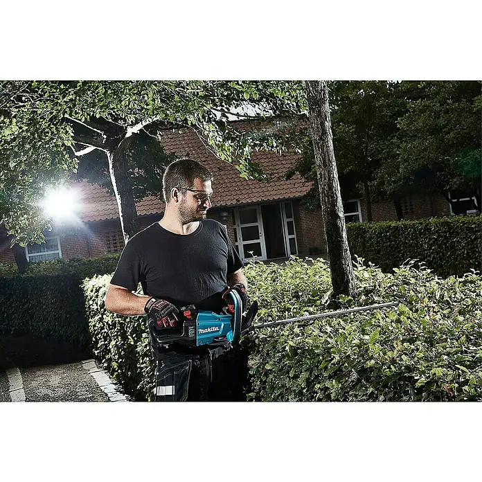 Makita LXT 18V Akku-Heckenschere DUH502Z - 18 V, Li-Ionen, Ohne Akku, Schnittlänge: 50 cm - Ein Mann, der mit einer Makita Heckenschere eine Hecke schneidet, mit Sicherheitsbrille und Handschuhen für sicheres Arbeiten im Garten.
