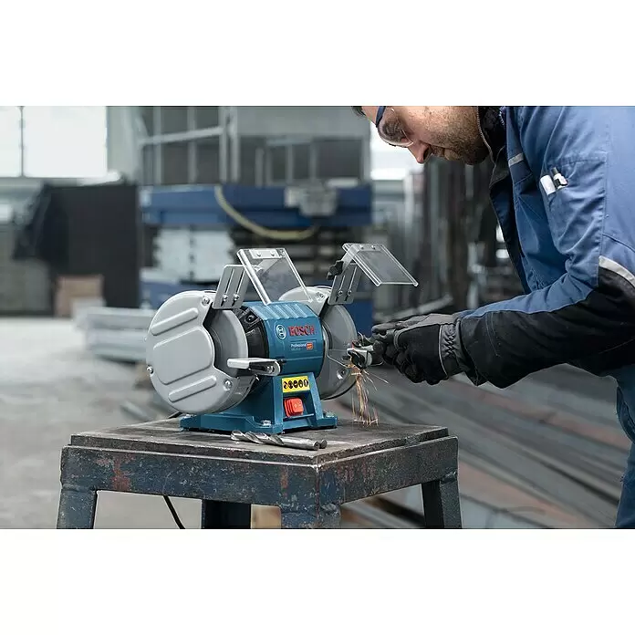 Bosch Professional Elektro-Doppelschleifer GBG 35-15 - 350 W, 3.000 U/min - Mann schärft Metall auf einem blau-grauen Bosch Doppelschleifer, Funken sprühen, an einem Tisch in einer Werkstatt.