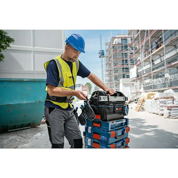 Bosch Professional Befestigungselement ProClick Holder - Passend für: Bosch Professional ProClick Gürteltaschen - Ein Bauarbeiter mit einem Bosch Werkzeugkoffer auf einer Baustelle, der Werkzeuge sortiert. Blaue Bosch Werkzeugkoffer sind praktisch für den Transport.