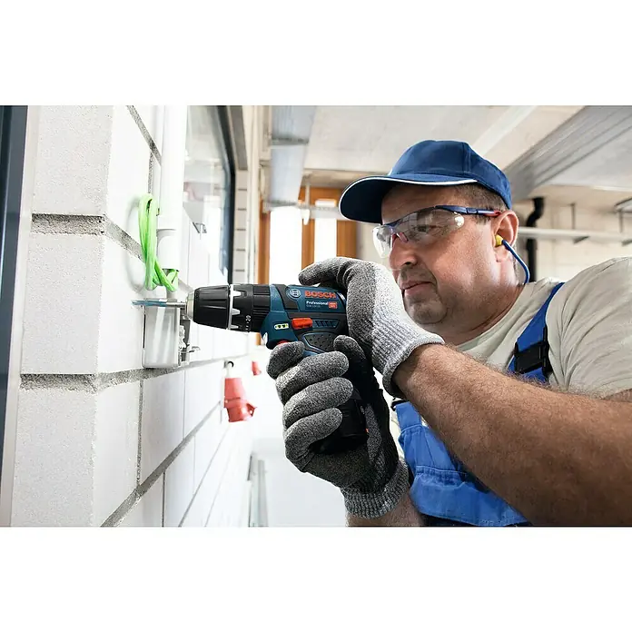 Bosch Professional Akku-Schlagbohrschrauber GSB 12V-15 - 12 V, 2 Akkus, 2 Ah, 30 Nm, 2 Akkus + Ladegerät + Bit-Set + Tasche - Nahaufnahme eines Handwerkers mit einer Bosch Professional Bohrmaschine, der an einer Wand arbeitet, mit Fokus auf das Werkzeug.