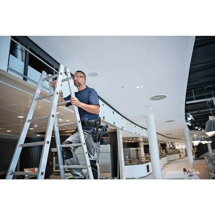 Bosch Professional Werkzeuggürtel-Set 935 -tlg. - Ein Handwerker steht auf einer Leiter und trägt einen Werkzeuggürtel mit Bosch-Werkzeugen in einem modernen Gebäude.