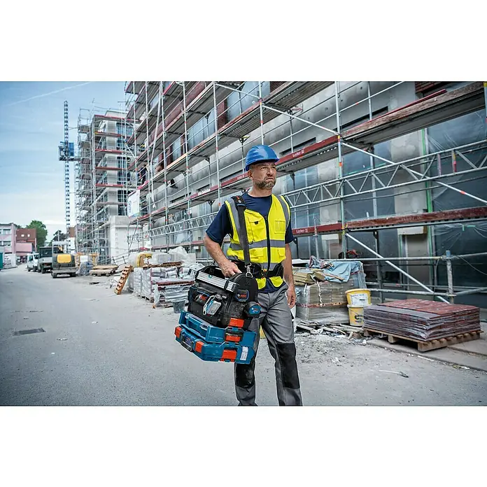 Bosch Professional Werkzeugtasche GWT 20 - L x B x H: 50 x 30 x 35 cm - Ein Bauarbeiter mit einem Bosch Werkzeugkoffer vor einer Baustelle. Der Koffer ist voll mit Werkzeugen für den täglichen Gebrauch.