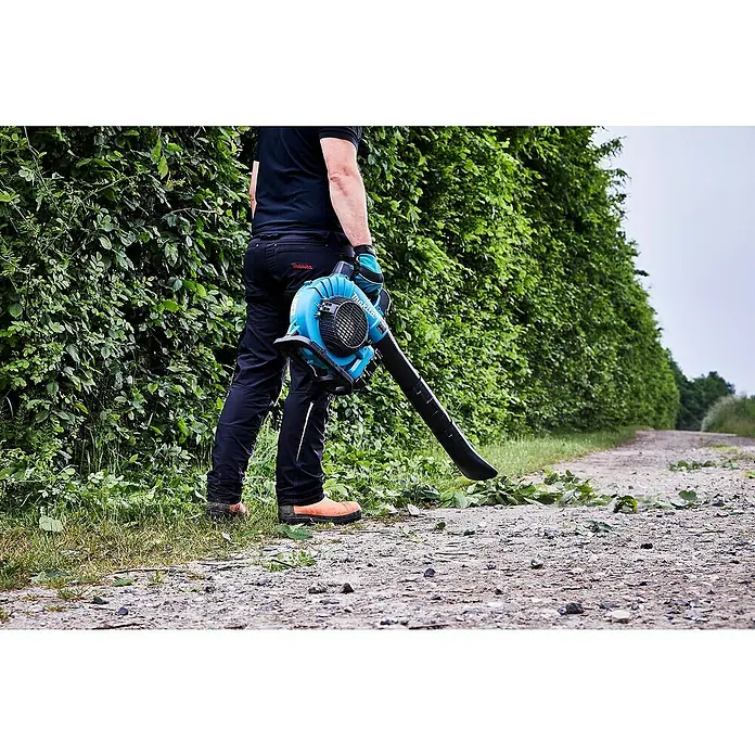 Makita LXT 18V Akku-Laubbläser DUB363PT2V - 18 V, Li-Ionen, 2 Akkus, Blasleistung: 13,4 m³/min - Ein Mann benutzt einen Makita Akku-Laubbläser, um Laub von einem Weg zu entfernen, mit üppigem Grün im Hintergrund.