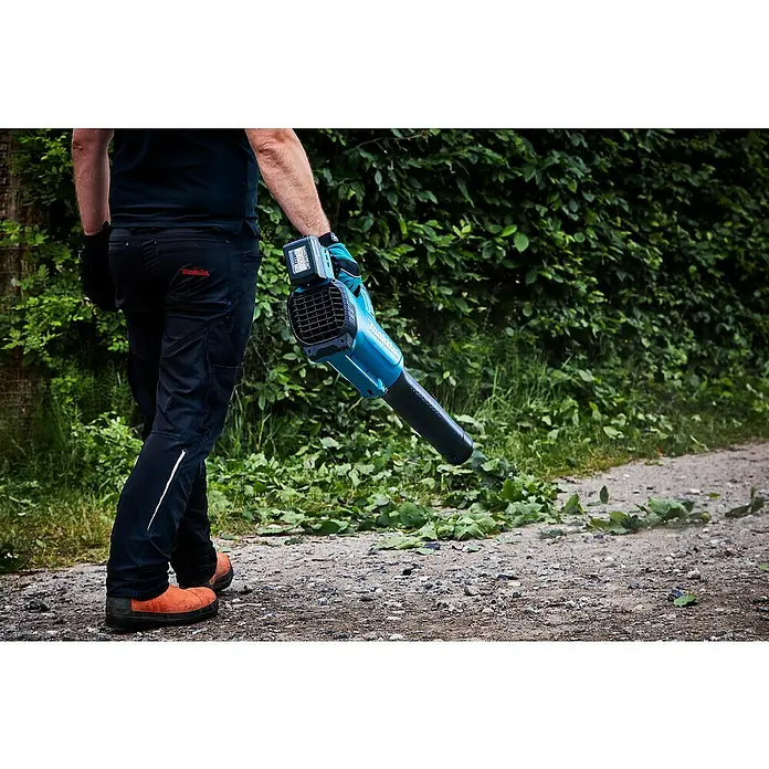 Makita LXT 18V Akku-Gebläse DUB184Z - 18 V, Ohne Akku, Blasgeschwindigkeit: 52,1 m/s - Eine Person benutzt einen Makita Akku-Laubbläser, um Blätter und kleine Äste von einem Weg zu blasen. Der Laubbläser ist blaugrün und schwarz.