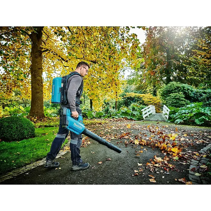 Makita LXT 18V Akku-Gebläse DUB184Z - 18 V, Ohne Akku, Blasgeschwindigkeit: 52,1 m/s - Ein Mann benutzt einen Makita Akku-Laubbläser im Freien, um Blätter zu entfernen, mit Akku-Rucksack für längere Laufzeit.