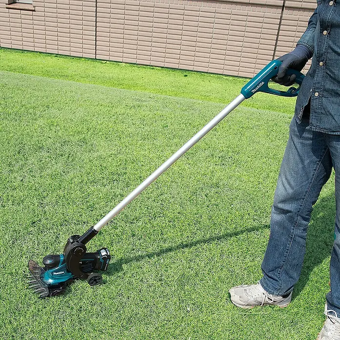 Makita Akku-Gras- & Strauchschere UM600DSMEX - 12 V, Li-Ionen, 1 Akku - Ein Mann benutzt einen Makita Rasenlüfter auf einer grünen Rasenfläche, um den Rasen zu pflegen. Das Gerät hat einen langen Griff und Räder.