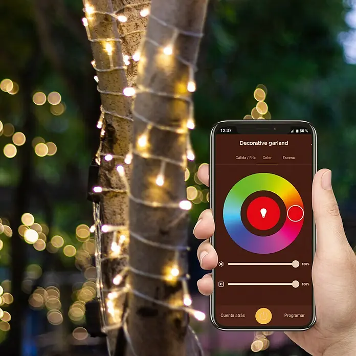 Muvit iO Guirnalda luminosa LED WiFi RGB+CCT - 6 m, Color de luz: RGBW, Para exterior - Primer plano de luces de cadena en un árbol, controladas a través de una aplicación de teléfono inteligente para la selección de color para la iluminación decorativa.