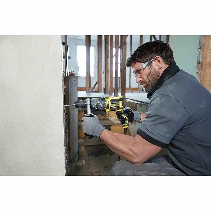 Stanley FatMax Schlagbohrmaschine FMEH850K-QS - 850 W, Schnellspannbohrfutter - Mann mit Schutzbrille und Handschuhen bohrt mit einem gelb-schwarzen Stanley FatMax Bohrhammer in eine Wand.