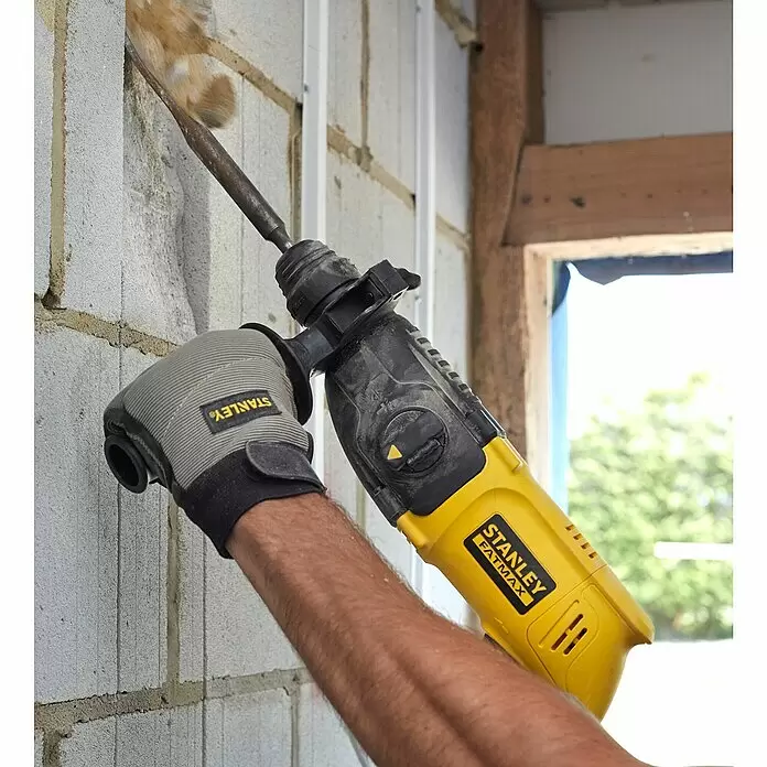 Stanley FatMax Kombihammer SFMEH200K-QS - 750 W, 2,2 J, SDS-Plus-Aufnahme - Person benutzt einen gelb-schwarzen Stanley Fatmax Bohrhammer mit Meißel, um eine Betonblockwand zu bearbeiten, Handschuhe tragend.