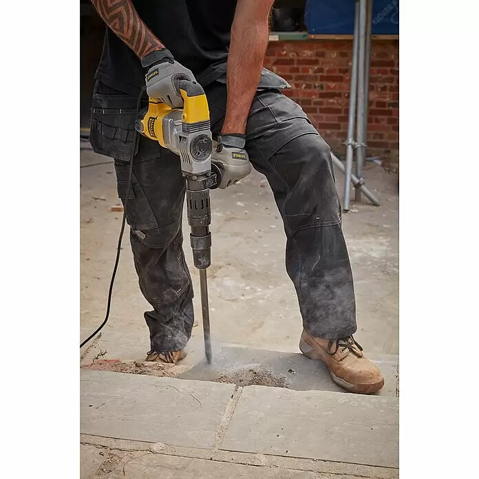 Stanley FatMax Abbruchhammer SFMEH220K-QS - 1.010 W, 8,5 J, SDS-Max-Aufnahme - Person in Arbeitshandschuhen und -hose benutzt einen gelb-grauen Abbruchhammer, um Betonpflaster zu brechen.