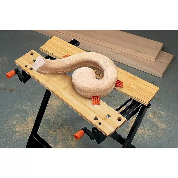 Black+Decker Werkbank Workmate® 301 - Belastbarkeit: 160 kg - Holzwerkbank mit schwarzen Beinen und orangefarbenen Griffen, die ein gebogenes Holzstück mit orangefarbenen Klemmen fixiert. Holzbretter daneben.