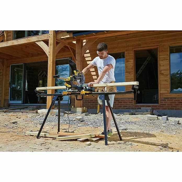 Stanley FatMax Kapp- & Gehrungssäge FME721-QS - 1.500 W, Durchmesser Sägeblatt: 216 mm, Leerlaufdrehzahl: 0 U/min - 5.000 U/min - Mann benutzt eine gelb-schwarze Gehrungssäge auf einem Ständer, um ein Holzbrett auf einer Baustelle zu sägen.