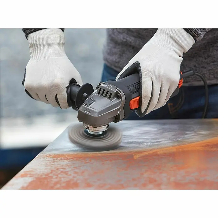 Black+Decker Elektro-Winkelschleifer BEG220-QS - 900 W, Durchmesser Scheibe: 125 mm, Leerlaufdrehzahl: 12.000 U/min - Nahaufnahme eines Winkelschleifers, der von einer Person mit Handschuhen auf einer Metalloberfläche verwendet wird.