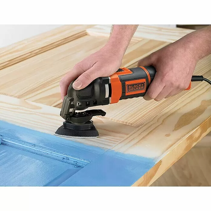 Black+Decker Elektro-Multifunktionswerkzeug MT300KA-QS - 300 W - Eine Person schleift mit einem schwarz-orangen Black+Decker Oszillationswerkzeug blaue Farbe von einer Holztür.