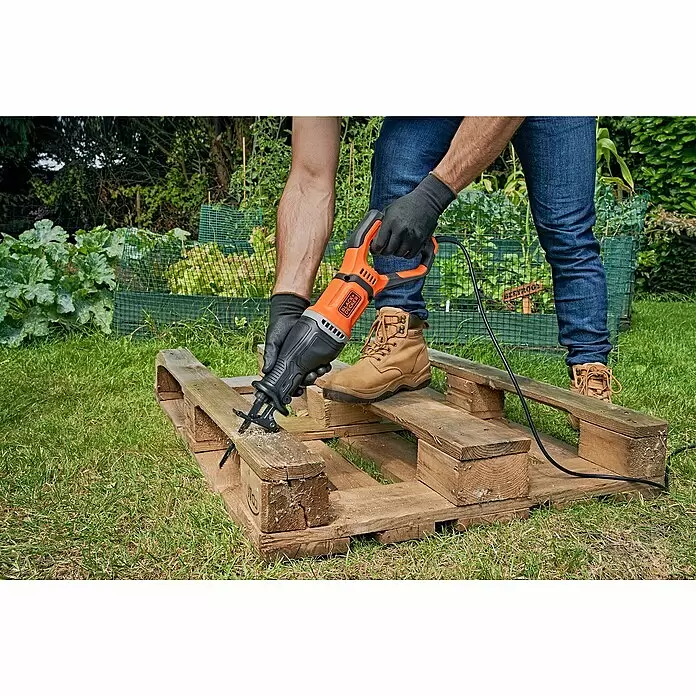 Black+Decker Säbelsäge BES301-QS - 750 W - Eine Person verwendet eine orange-schwarze Säbelsäge, um eine Holzpalette im Garten zu zersägen.