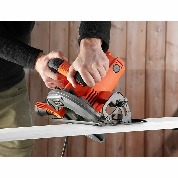 Black+Decker Handkreissäge CS1550-QS - 1.500 W, Durchmesser Sägeblatt: 190 mm, Schnitttiefe bei 90 °: 66 mm - Der Mann schneidet mit einer Black+Decker Kreissäge ein weißes Brett vor einer Holzwand.
