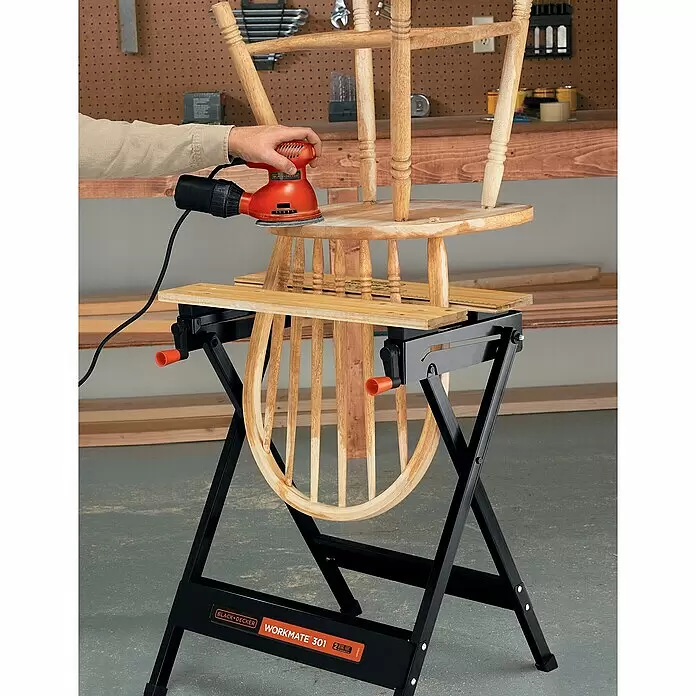 Black+Decker Werkbank Workmate® 301 - Belastbarkeit: 160 kg - Schwarze Black+Decker Workmate 301 Werkbank hält einen Holzstuhl, der mit einem orangefarbenen Schleifer bearbeitet wird.
