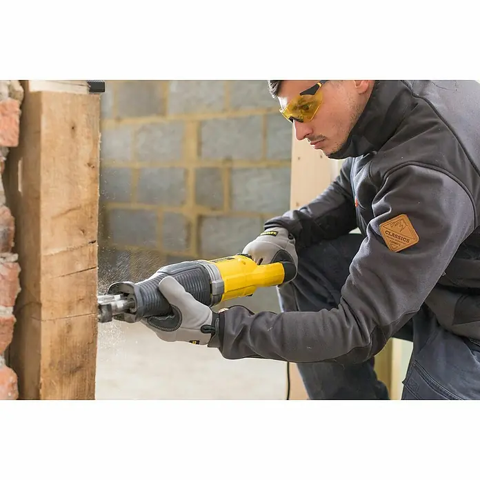 Stanley FatMax Säbelsäge FME360-QS - 900 W, Hublänge: 28 mm - Ein Handwerker in Schutzbrille verwendet eine gelbe Säbelsäge, um ein Stück Holz zu schneiden, wobei er Handschuhe und eine Jacke trägt.