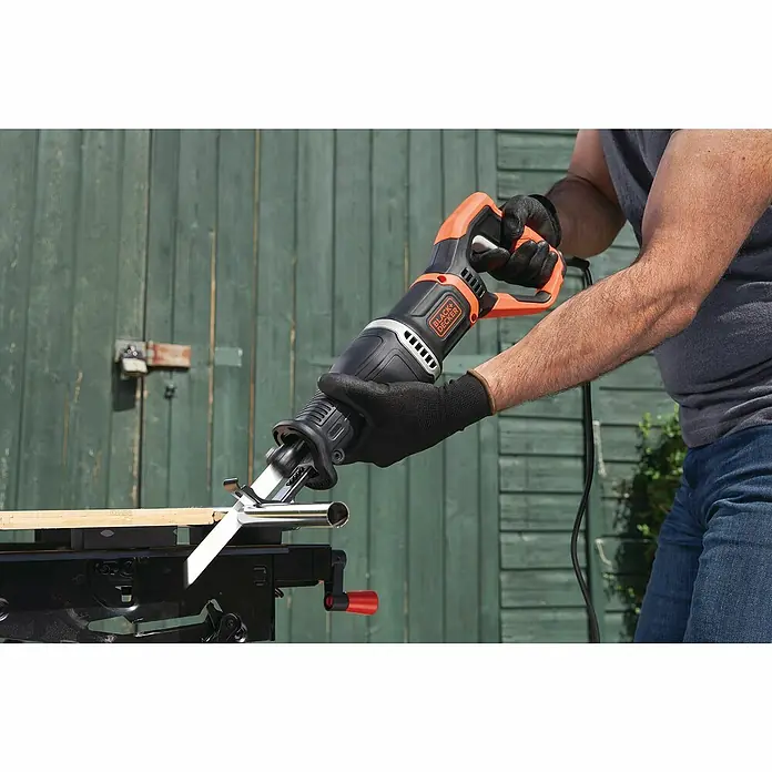 Black+Decker Säbelsäge BES301-QS - 750 W - Eine Black+Decker Säbelsäge schneidet ein Metallrohr auf einer Werkbank, wobei der Bediener Handschuhe und Schutzkleidung trägt.