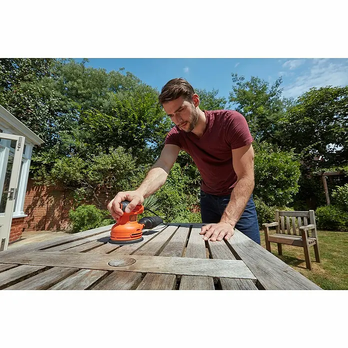 Black+Decker Elektro-Exzenterschleifer BEW210-QS - 230 W, Durchmesser Schleifteller: 125 mm - Ein Mann benutzt einen Black+Decker Schleifer, um einen Holztisch im Freien abzuschleifen.