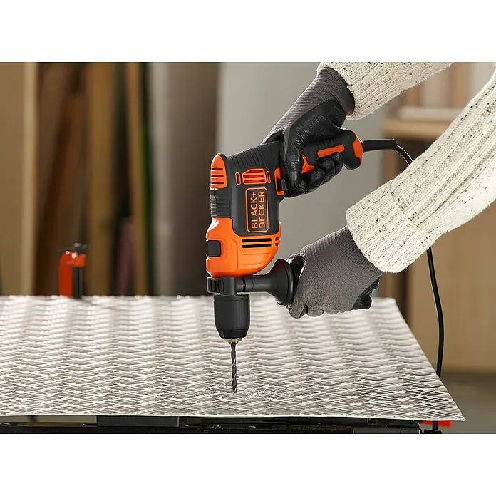 Black+Decker Schlagbohrmaschine BEH550K-QS - 550 W, Schnellspannbohrfutter - Ein Black+Decker-Bohrer wird von einer Person verwendet, die Handschuhe trägt und ein Loch in ein Metallstück bohrt.