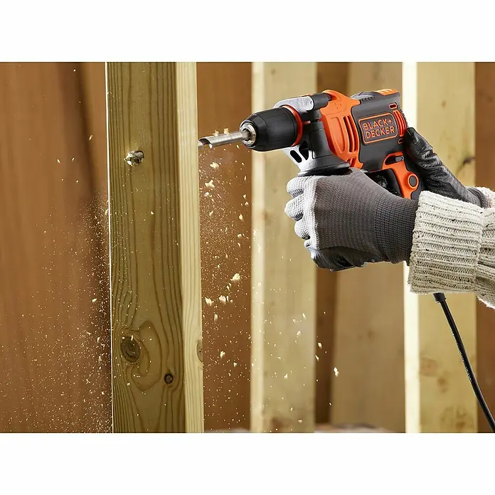 Black+Decker Schlagbohrmaschine BEH550K-QS - 550 W, Schnellspannbohrfutter - Eine Black+Decker Bohrmaschine wird zum Bohren in Holz verwendet, wobei Holzspäne herumfliegen.