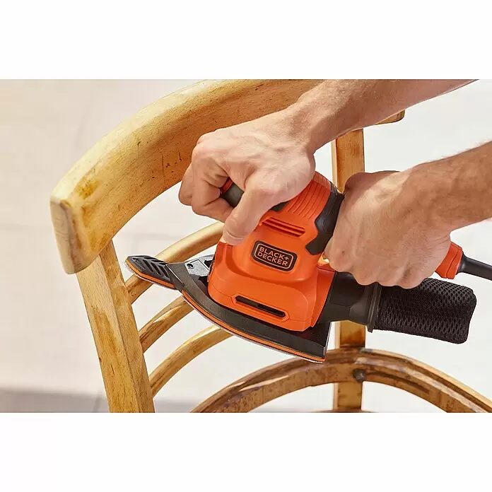 Black+Decker Elektro-Multischleifer BEW200K-QS - 200 W, Leerlaufschwingzahl: 24.000 U/min, Durchmesser Schwingkreis: 2 mm - Eine Person schleift mit einem orange-schwarzen Black+Decker Schleifer die Oberfläche eines Holzstuhls.