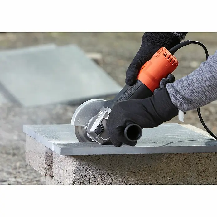 Black+Decker Elektro-Winkelschleifer BEG220-QS - 900 W, Durchmesser Scheibe: 125 mm, Leerlaufdrehzahl: 12.000 U/min - Winkelschleifer beim Schneiden einer Steinplatte. Die Person trägt schwarze Handschuhe für zusätzlichen Schutz.