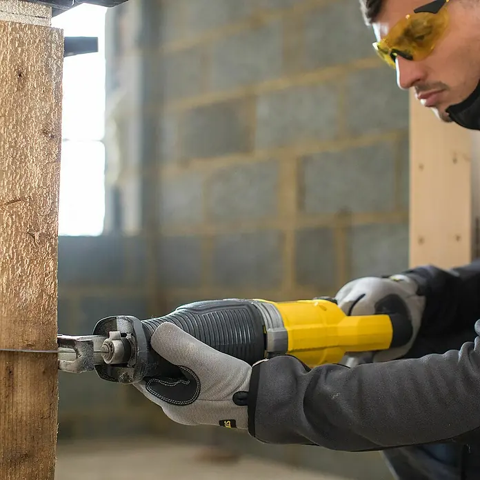 Stanley FatMax Säbelsäge FME360-QS - 900 W, Hublänge: 28 mm - Ein Mann sägt ein Holzbrett mit einer gelben Säbelsäge. Der Fokus liegt auf der Säge, die durch das Holz schneidet, und der Schutzausrüstung des Mannes.