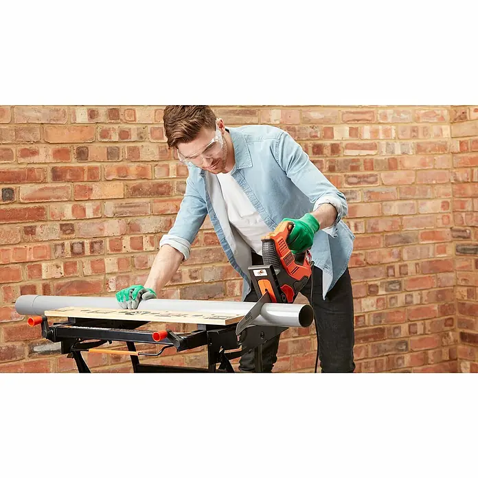 Black+Decker Elektro-Stichsäge RS890K-QS - 500 W, Hublänge: 23 mm - Ein Mann sägt ein Rohr mit einer BLACK+DECKER Säbelsäge, umgeben von einer Backsteinmauer. Er trägt Schutzkleidung für die Arbeit.