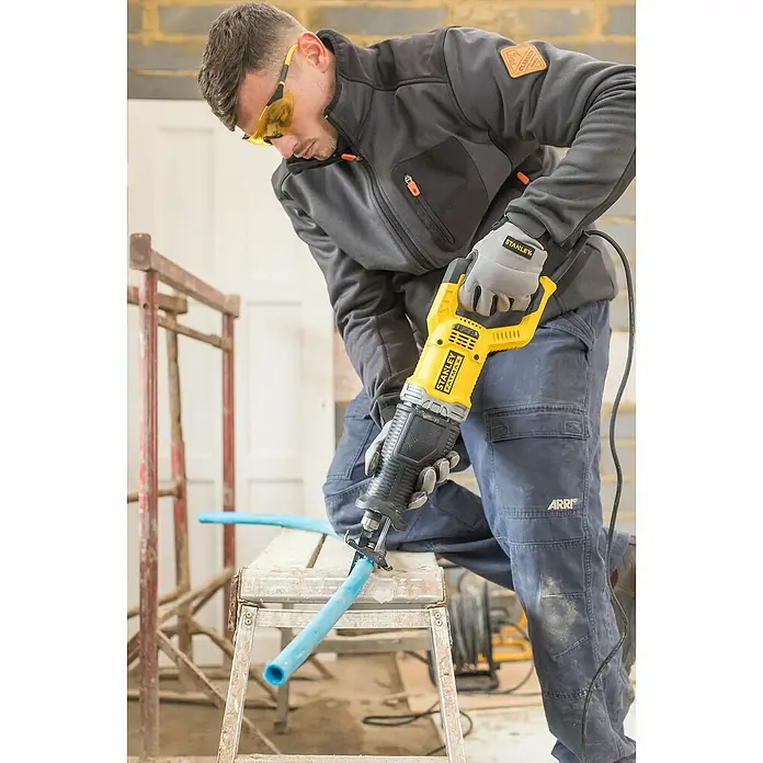 Stanley FatMax Säbelsäge FME360-QS - 900 W, Hublänge: 28 mm - Ein Mann benutzt eine Stanley Säbelsäge, um ein blaues Rohr zu schneiden, während er Schutzkleidung trägt.