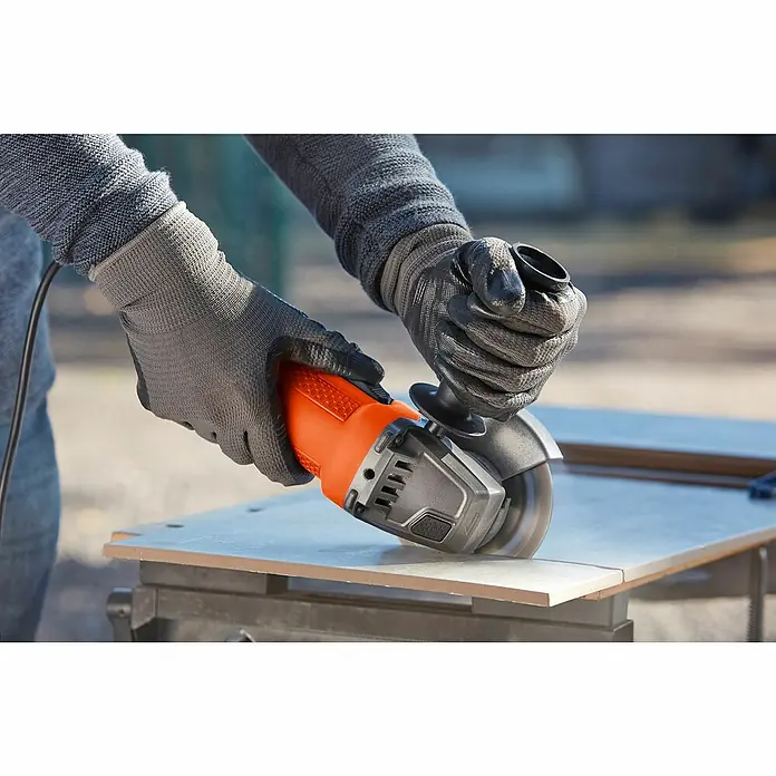 Black+Decker Elektro-Winkelschleifer BEG110-QS - 750 W, 115 mm - Eine Person benutzt einen Black+Decker Winkelschleifer, um eine Fliese zu schneiden. Der Winkelschleifer ist orange und schwarz.