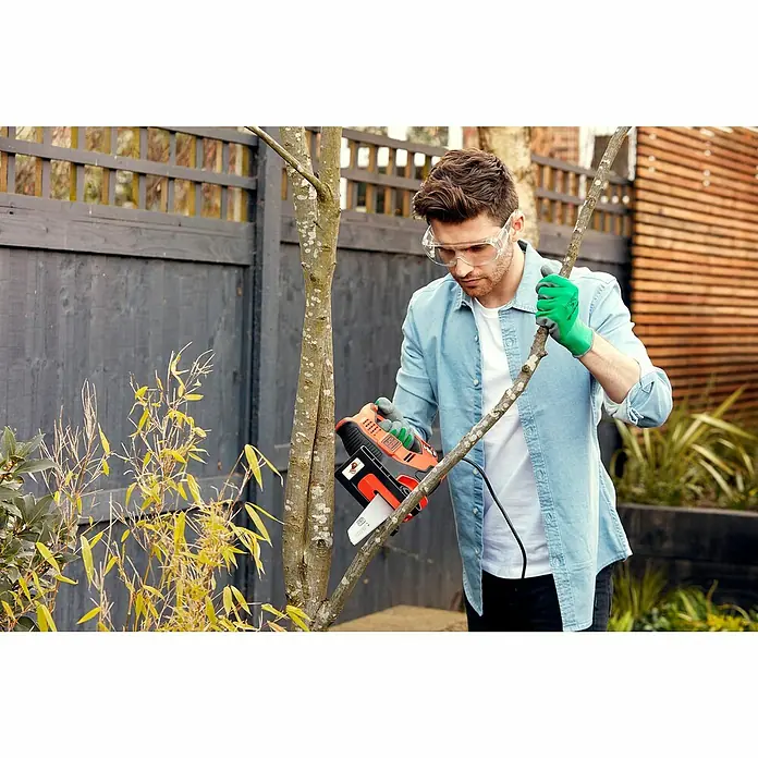 Black+Decker Elektro-Stichsäge RS890K-QS - 500 W, Hublänge: 23 mm - Ein Mann benutzt eine Akku-Astsäge von Black+Decker, um einen Ast im Garten zu schneiden. Schutzkleidung wird getragen.
