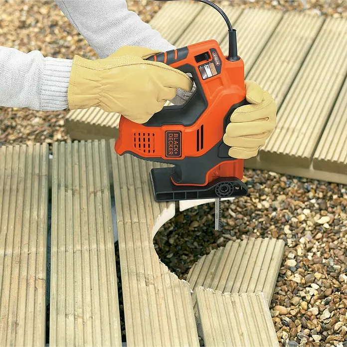 Black+Decker Elektro-Stichsäge RS890K-QS - 500 W, Hublänge: 23 mm - Nahaufnahme einer Black+Decker Stichsäge beim Schneiden eines Holzstücks, bedient von einer Person mit Handschuhen, im Freien.