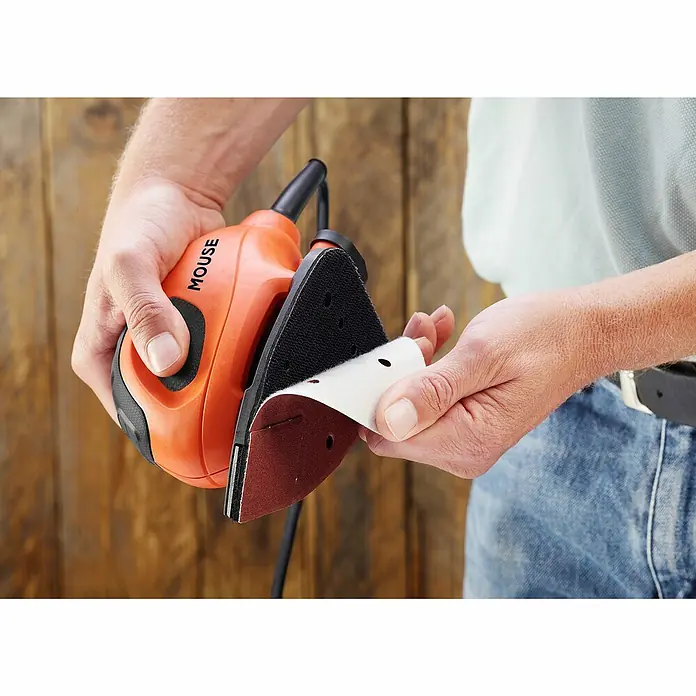 Black+Decker Elektro-Multischleifer BEW230K-QS - 55 W, Leerlaufschwingzahl: 22.000 U/min, Durchmesser Schwingkreis: 1,5 mm - Nahaufnahme einer Hand, die Schleifpapier an einer orangefarbenen "Mouse"-Schleifmaschine befestigt.