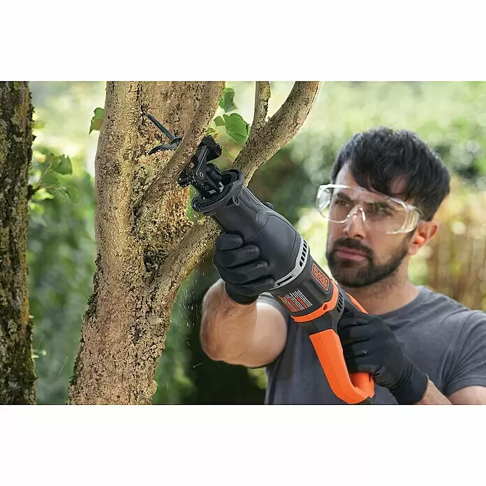 Black+Decker Säbelsäge BES301-QS - 750 W - Ein Mann in Schutzkleidung benutzt eine schwarz-orangefarbene BLACK+DECKER Säbelsäge, um einen Ast zu schneiden, wobei Holzstaub entsteht.
