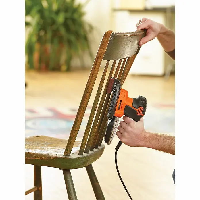 Black+Decker Elektro-Multischleifer KA2000-QS - 120 W, Leerlaufschwingzahl: 1.400 U/min, Durchmesser Schwingkreis: 2 mm - Detailaufnahme eines Black+Decker Schleifgeräts beim Bearbeiten eines Holzstuhls. Perfekt für Möbelrestaurierung und DIY-Projekte.