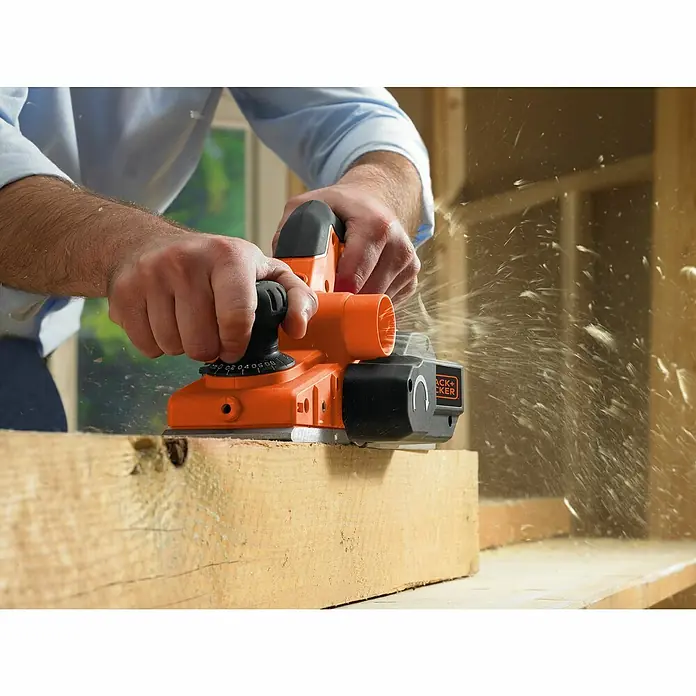 Black+Decker Elektrohobel KW750K-QS - 750 W, Hobeltiefe: 0 mm - 2 mm, Leerlaufdrehzahl: 16.500 U/min - Ein Handwerker benutzt einen Black+Decker Hobel auf einem Holzbrett, um es zu bearbeiten. Späne fliegen dabei umher.