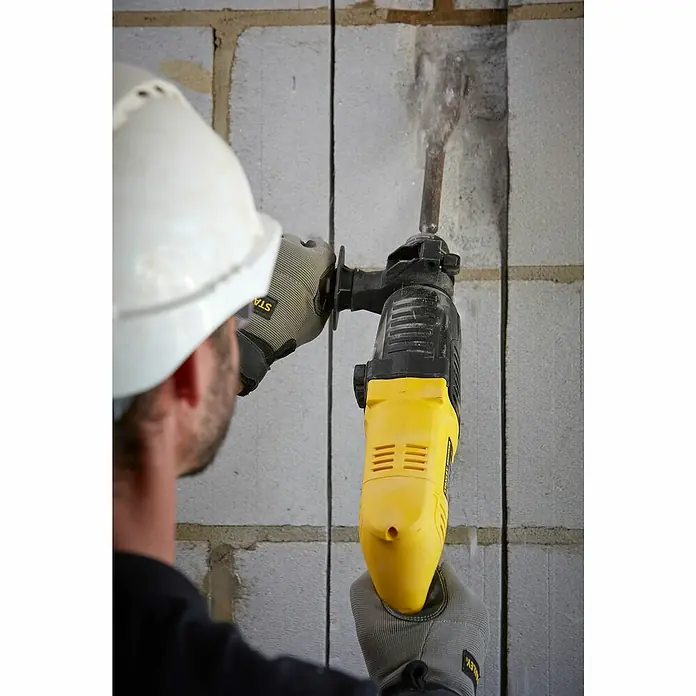 Stanley FatMax Kombihammer SFMEH200K-QS - 750 W, 2,2 J, SDS-Plus-Aufnahme - Nahaufnahme eines Bauarbeiters mit Schutzhelm, der mit einem gelb-schwarzen Stanley-Bohrhammer in eine Ziegelwand bohrt.