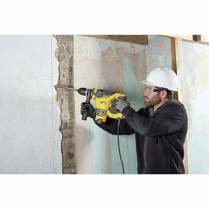 Stanley FatMax Kombihammer FME1250K-QS - 1.250 W, 3,5 J, SDS-Plus-Aufnahme - Ein Bauarbeiter benutzt einen gelben Stanley Fatmax Bohrhammer mit Schutzbrille und Helm an einer Baustelle.