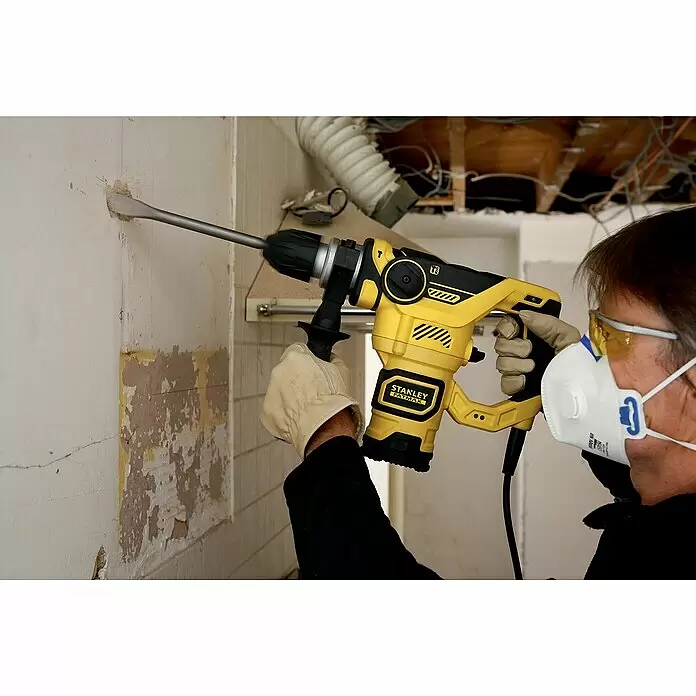 Stanley FatMax Kombihammer FME1250K-QS - 1.250 W, 3,5 J, SDS-Plus-Aufnahme - Person benutzt gelb-schwarzen Stanley Fatmax Bohrhammer zum Meißeln einer Wand bei Renovierungsarbeiten, trägt Schutzkleidung.