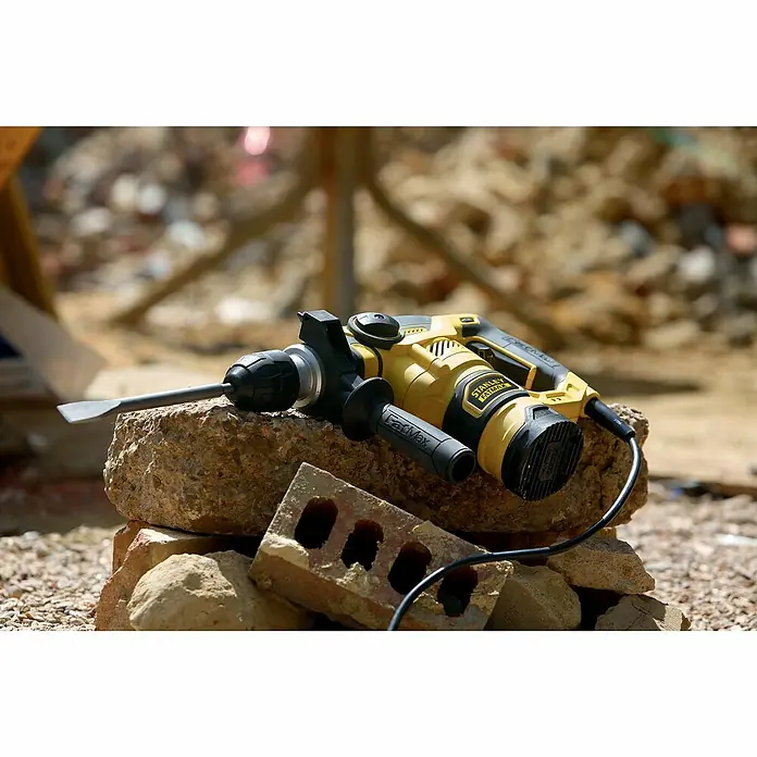 Stanley FatMax Kombihammer FME1250K-QS - 1.250 W, 3,5 J, SDS-Plus-Aufnahme - Nahaufnahme eines gelben Stanley Fatmax Abbruchhammers auf einem Steinhaufen im Freien.