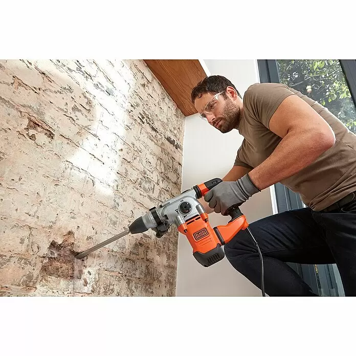 Black+Decker Kombihammer BEHS03K-QS - 1.250 W, 3,7 J, SDS-Plus-Aufnahme - Ein Mann benutzt einen orange-silbernen Black+Decker Bohrhammer, um in eine Ziegelwand zu bohren.