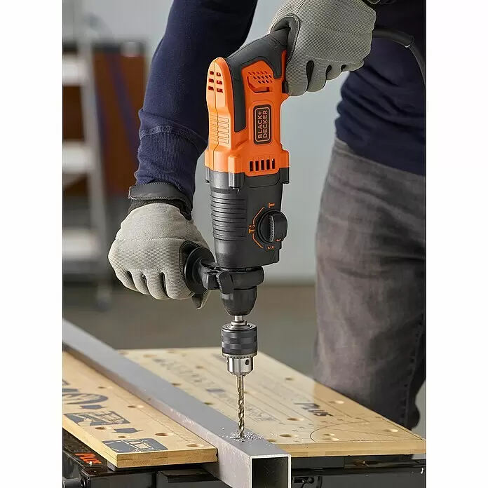 Black+Decker Kombihammer BEHS01K-QS - 650 W, 1,4 J, SDS-Plus-Aufnahme - Person bohrt mit einem orange-schwarzen Black+Decker Schlagbohrer in einen Metallträger auf einer Werkbank.