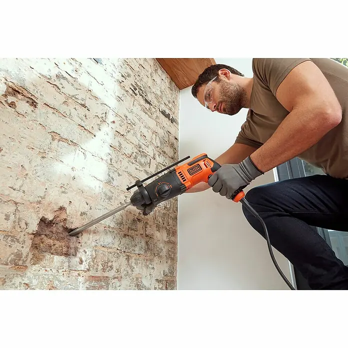 Black+Decker Kombihammer BEHS01K-QS - 650 W, 1,4 J, SDS-Plus-Aufnahme - Ein Mann bohrt mit einer Black+Decker Bohrmaschine ein Loch in eine Ziegelwand, wobei er eine Schutzbrille und Handschuhe trägt.