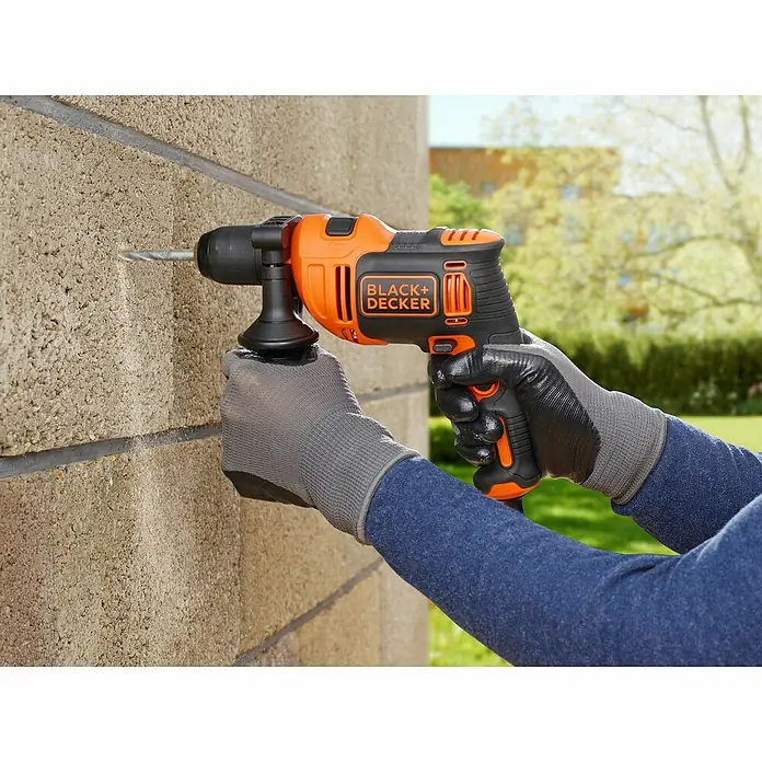 Black+Decker Schlagbohrmaschine BEH710K-QS - 710 W, 2.800 U/min, Max. Schlagzahl: 47.600 /min - Eine orangefarbene Black+Decker Bohrmaschine wird von einer Person mit Arbeitshandschuhen benutzt, um ein Loch in eine Ziegelmauer zu bohren.