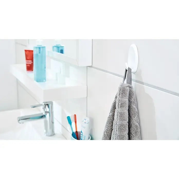 Tesa Powerstrips Selbstklebehaken - Oval, Größe: L, Chrom matt, 2 Stk. - Ein graues Handtuch hängt an einem weißen Wandhaken im Badezimmer. Im Hintergrund sind Waschtischarmatur und Pflegeprodukte zu sehen.