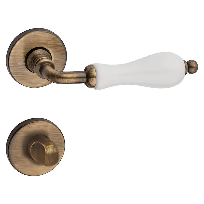 Diamond Doors Classic Zimmertürgarnitur WC Columbus - Bronze, Stärke Tür: 40 mm - 45 mm, Schlitzkopf/Olive - Detailaufnahme einer antiken Türgarnitur mit einer weißen Porzellanklinke und bronzefarbenen Beschlägen, die einen Vintage-Charme versprüht.
