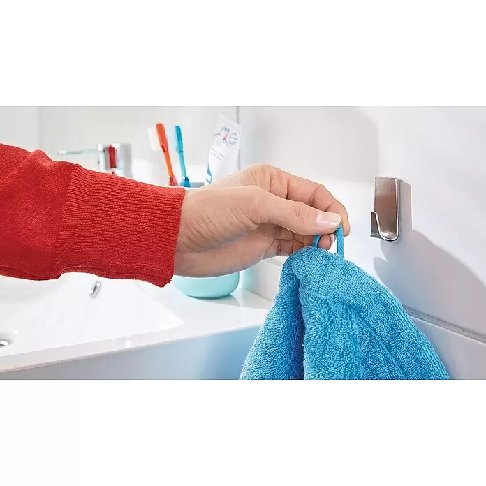 Tesa Powerstrips Selbstklebehaken - Rechteckig, Größe: S, Metallic, 2 Stk. - Eine Hand hängt ein blaues Handtuch mit Schlaufe an einen silbernen Metallhaken an einer weißen Badezimmerwand.