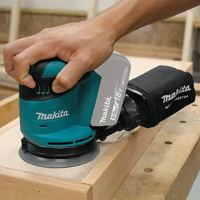Makita LXT 18V Akku-Exzenterschleifer DBO180Z - 18 V, Ohne Akku, Durchmesser Schleifteller: 125 mm - Nahaufnahme eines Makita Akku-Exzenterschleifers in Aktion, der auf einer Holzoberfläche verwendet wird.
